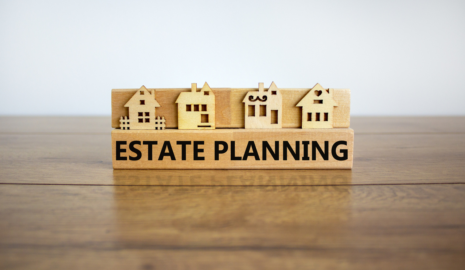 Wooden blocks form the words 'estate planning', miniature house, wooden table. Beautiful white background, copy space. Business and estate planning concept.